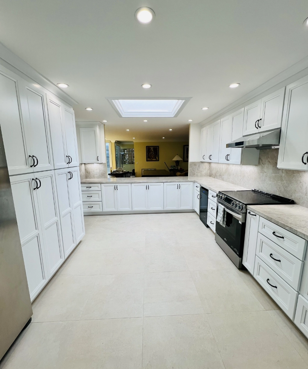 Spacious kitchen with white cabinets, a light countertop, and a skylight. Featuring stainless steel appliances and recessed lighting, this space exemplifies home remodeling at its finest.