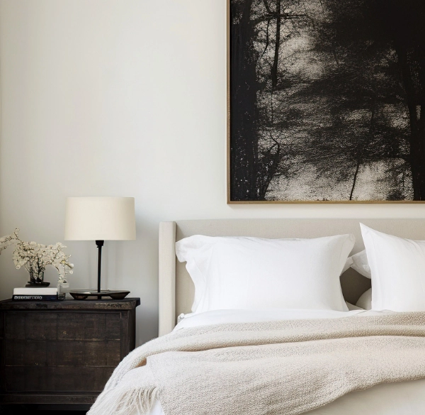 A primary bedroom with beige linens and artwork hung above the bed.