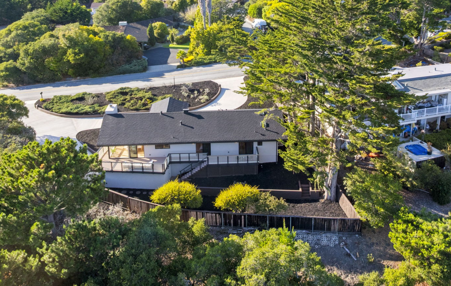 Aerial view of a single-story house with a black roof, surrounded by trees and greenery on a corner lot near a curved residential street—showcasing a Full Interior-Exterior Home Remodel in Carmel.