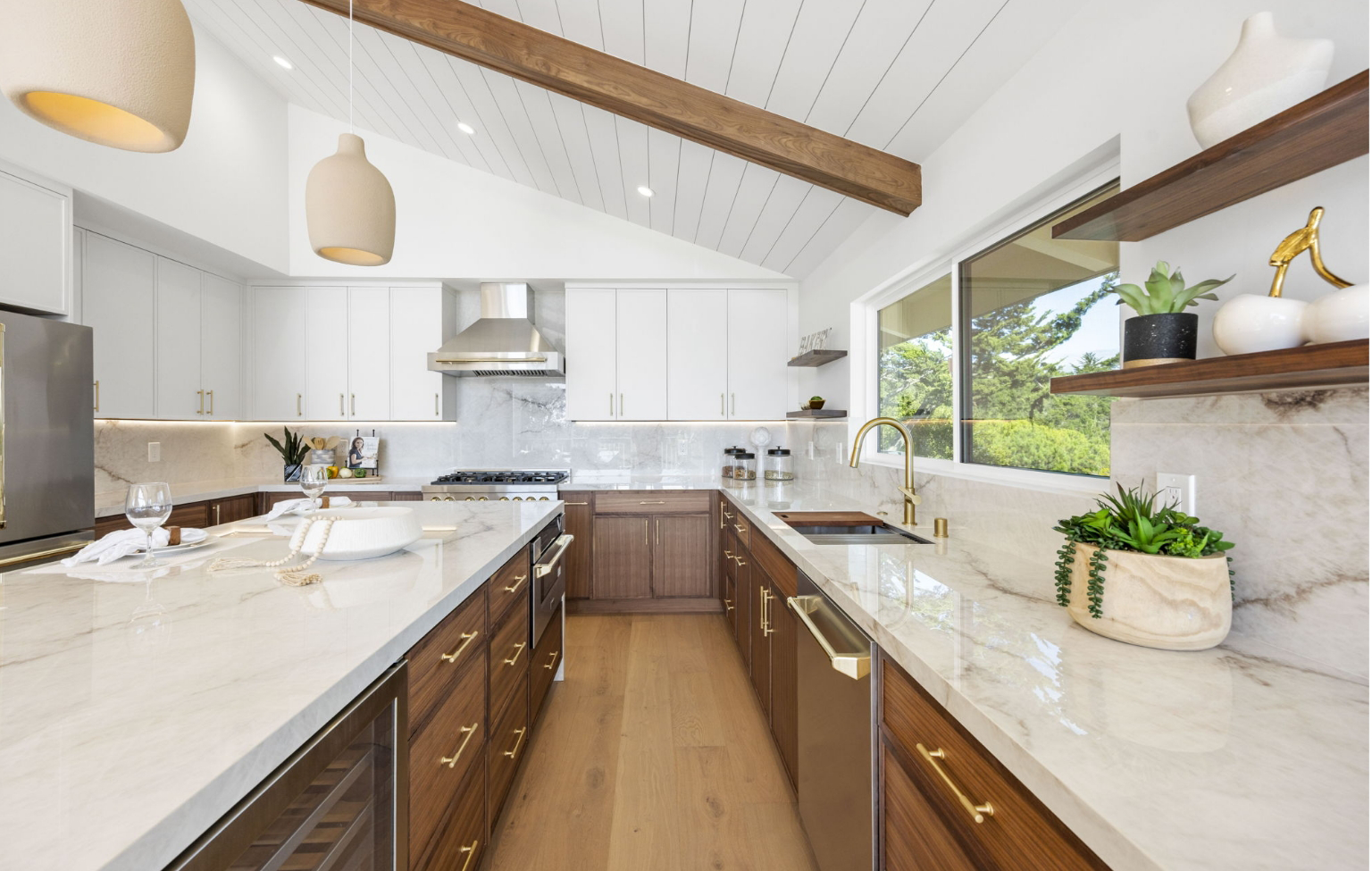 Modern kitchen with white cabinets, wood accents, marble countertops, stainless steel appliances, and pendant lights, part of a Full Interior-Exterior Home Remodel in Carmel, featuring a large window with an inviting outdoor view.