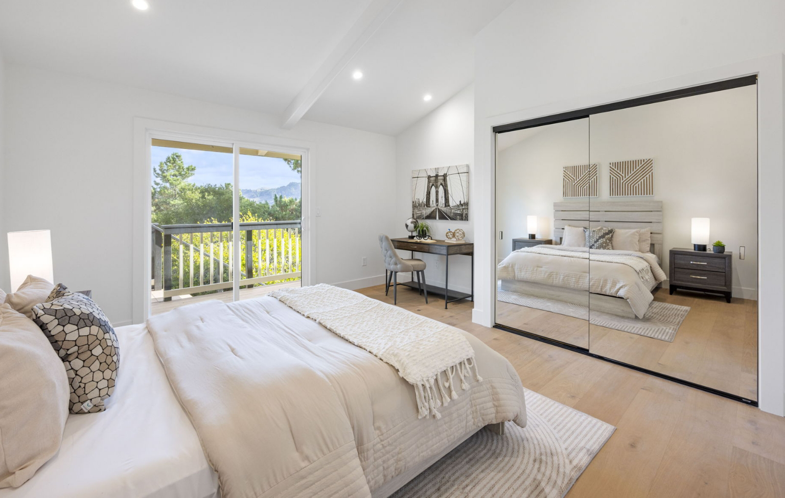 Bright bedroom with light wood floors, a large bed, mirrored closet doors, and sliding glass doors opening to a balcony with a view of greenery—part of a Full Interior-Exterior Home Remodel in Carmel.