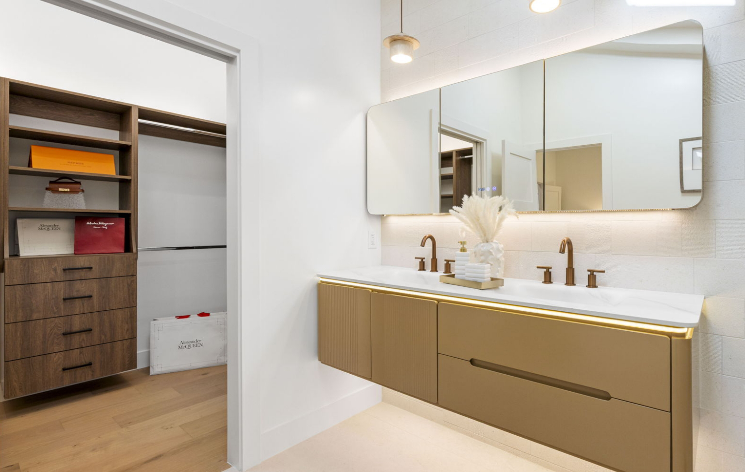 A modern bathroom with a double sink vanity, large mirror, and brown cabinets stands adjacent to a walk-in closet with shelves and luxury shopping bags—a highlight of this Full Interior-Exterior Home Remodel in Carmel.