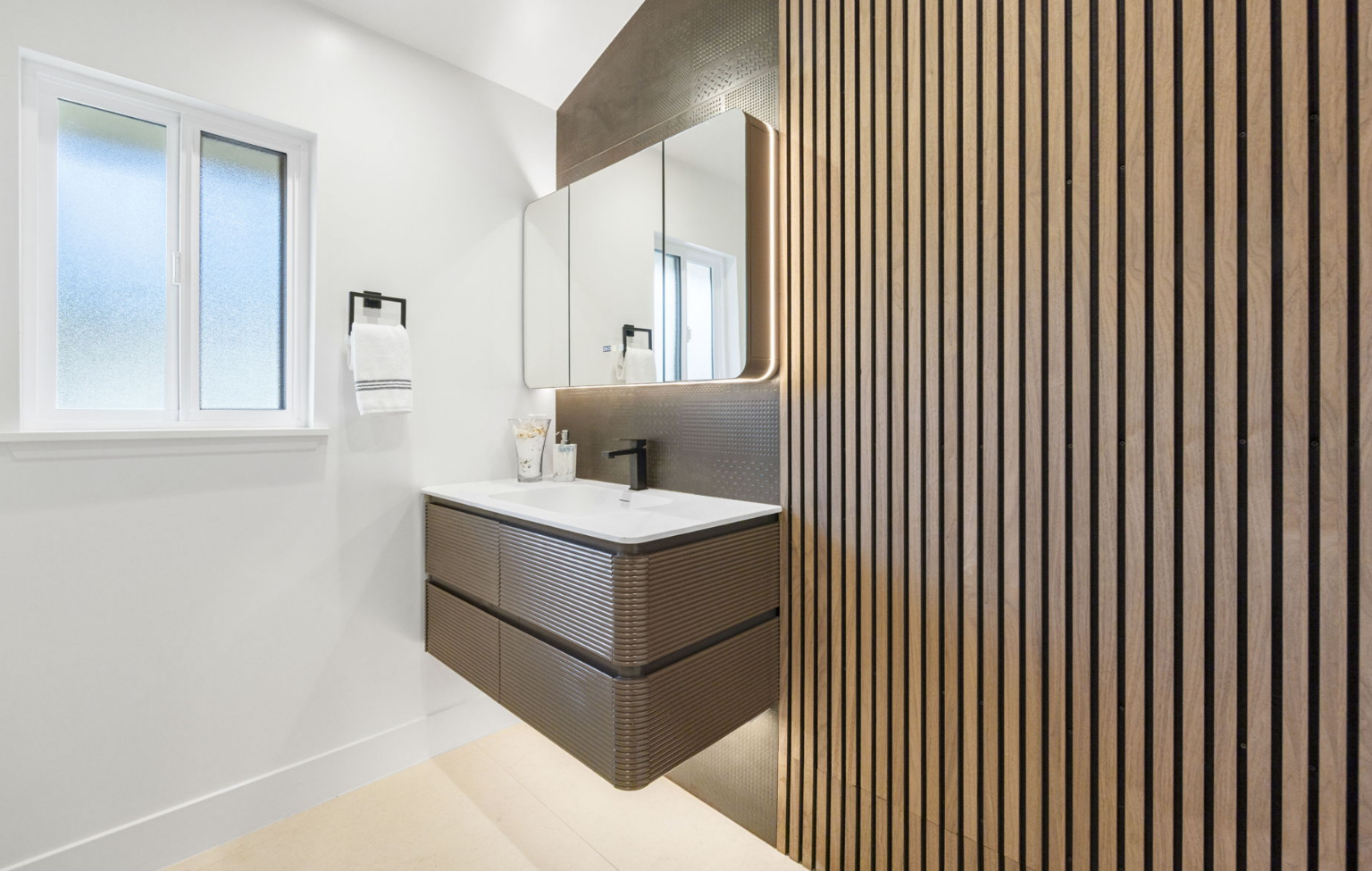 Modern bathroom with a floating vanity, rectangular mirror cabinet, wall-mounted faucet, towel rack, and wood slat accent wall as part of a Full Interior-Exterior Home Remodel in Carmel.