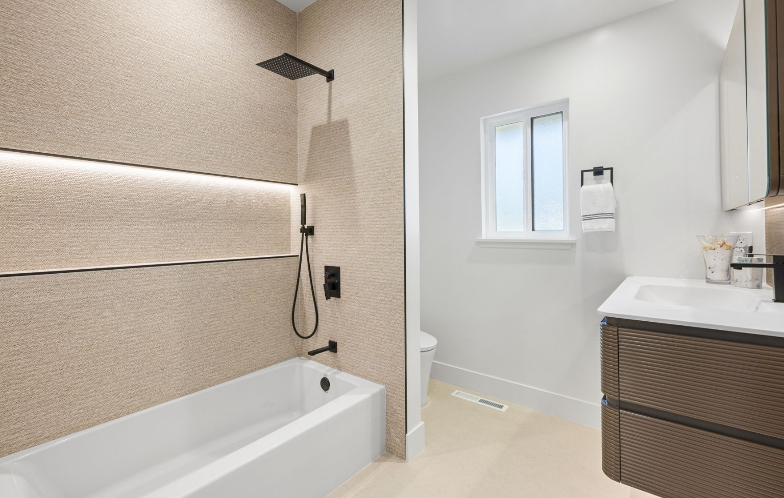 Modern bathroom from a Full Interior-Exterior Home Remodel in Carmel featuring a beige tiled bathtub-shower combo, black fixtures, wall-mounted vanity, white walls, and a window letting in natural light.