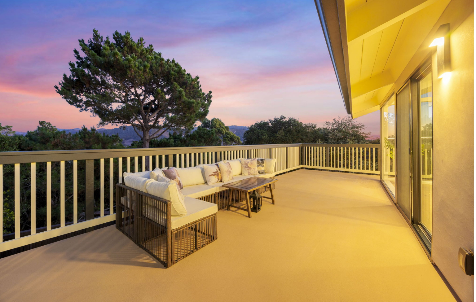 Spacious outdoor balcony with cushioned seating and a table, surrounded by a railing, overlooking trees at sunset—perfect for enjoying your Full Interior-Exterior Home Remodel in Carmel.