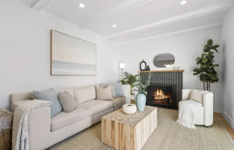 Modern living room with a beige sectional sofa, wooden coffee table, fireplace, armchair, potted plant, and minimalist decor—perfect inspiration for Bay Area remodeling projects.