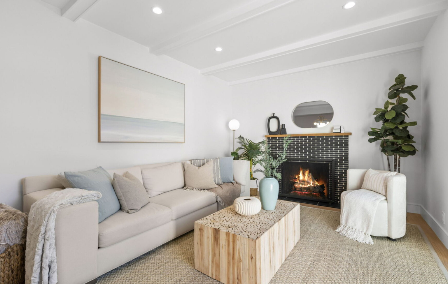 Modern living room with a beige sectional sofa, wooden coffee table, fireplace, armchair, potted plant, and minimalist decor—perfect inspiration for Bay Area remodeling projects.