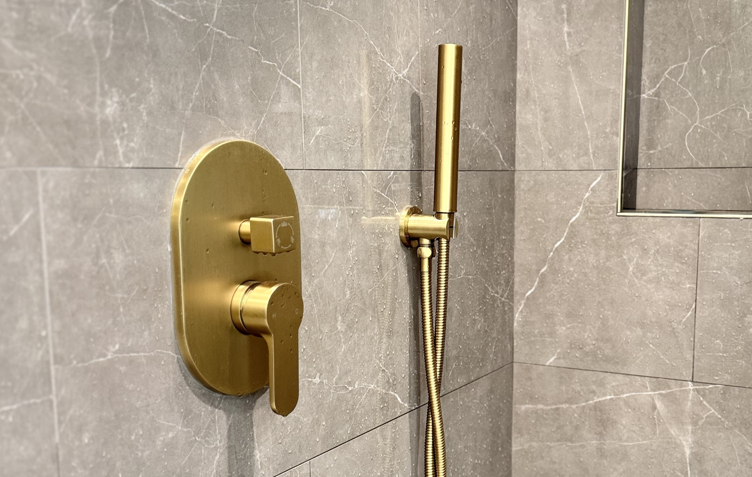 Gold handheld showerhead and control panel mounted on a gray marble-tiled bathroom wall, part of a stunning full interior remodel with custom kitchen in Danville.