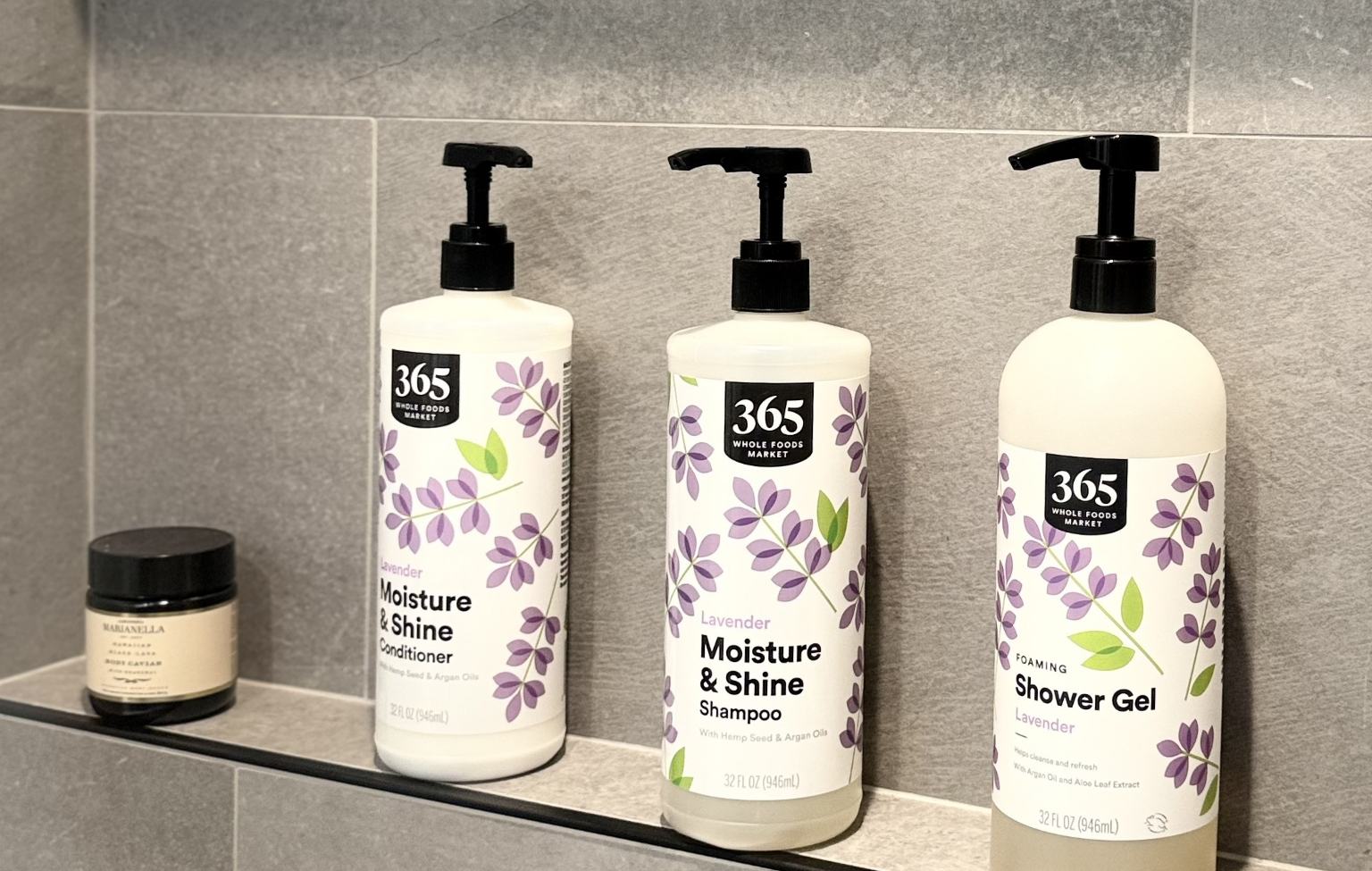 Four bath products, including three 365 brand bottles of conditioner, shampoo, and shower gel with lavender designs, and one small jar on a grey bathroom shelf—perfect accents after a Full Interior Remodel With Custom Kitchen in Danville.